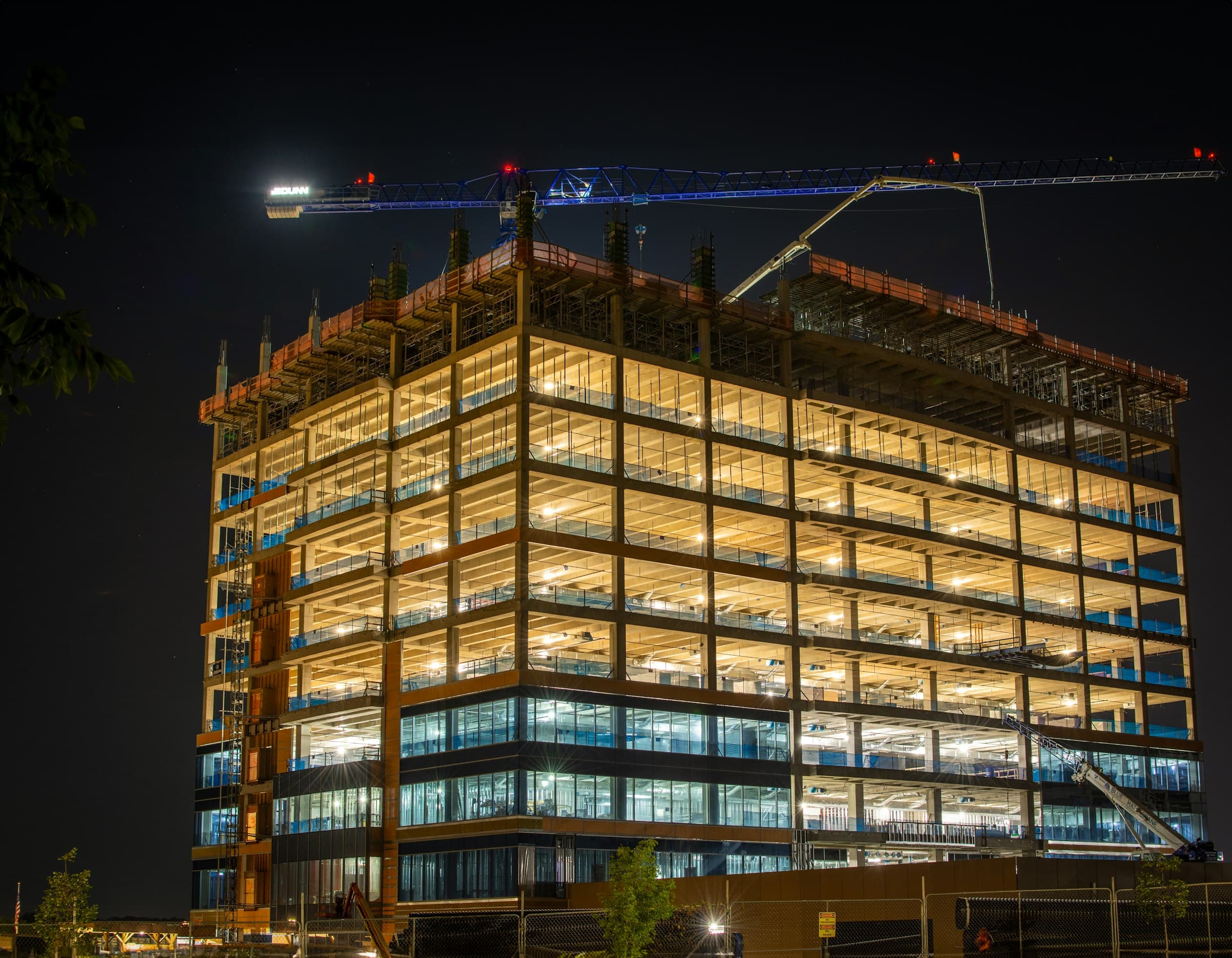 A building under construction lit floor by floor at night, a crane above it