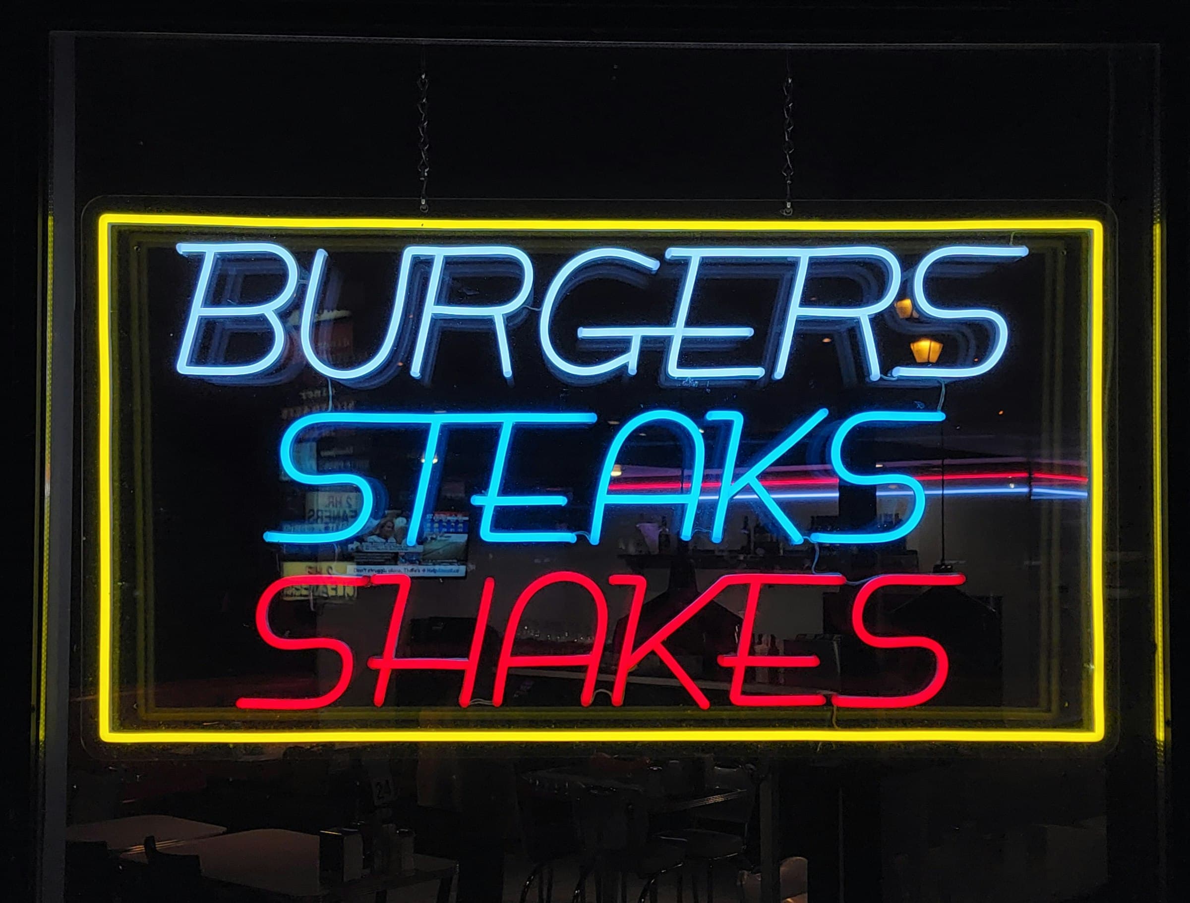 A neon sign in blue, red and yellow reading Burgers, Steaks, Shakes