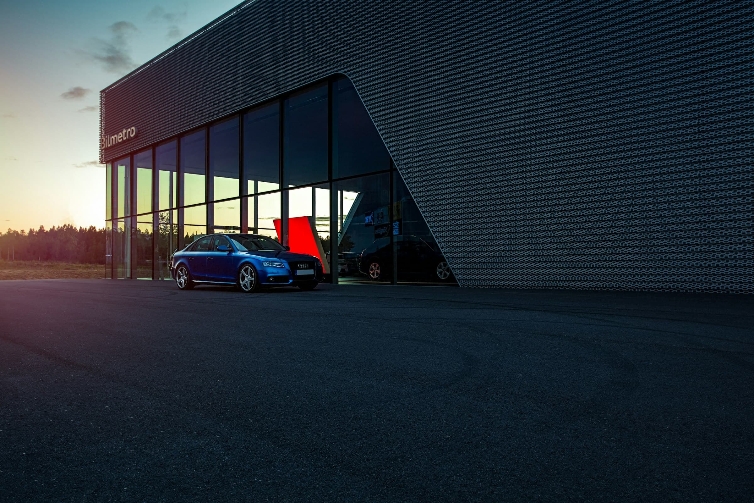 A car parked outside a dealership's glass showroom at dusk