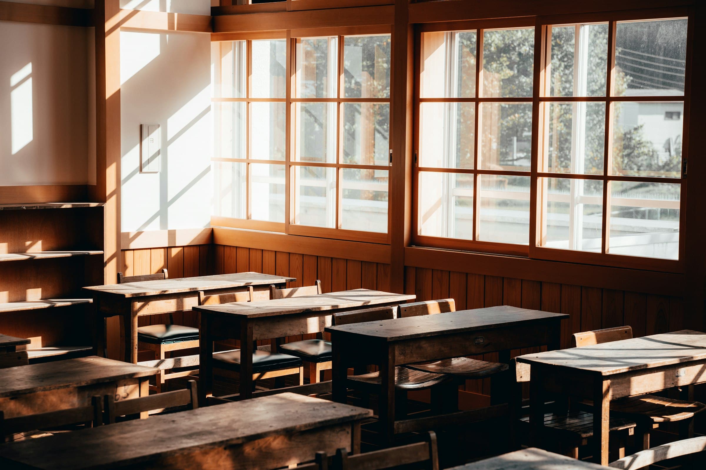 An empty wooden classroom lit by low golden sun through tall windows