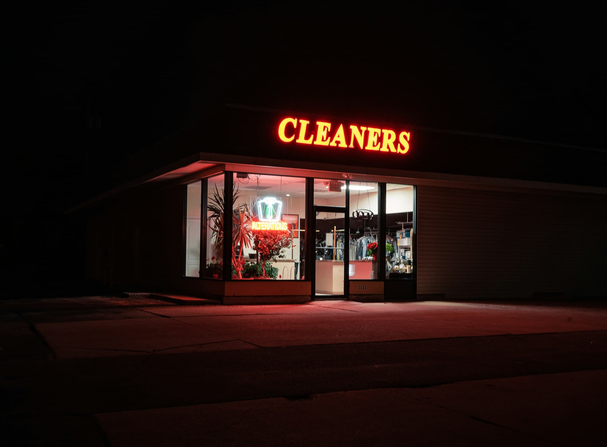 A dry cleaner's storefront at night under a red CLEANERS sign