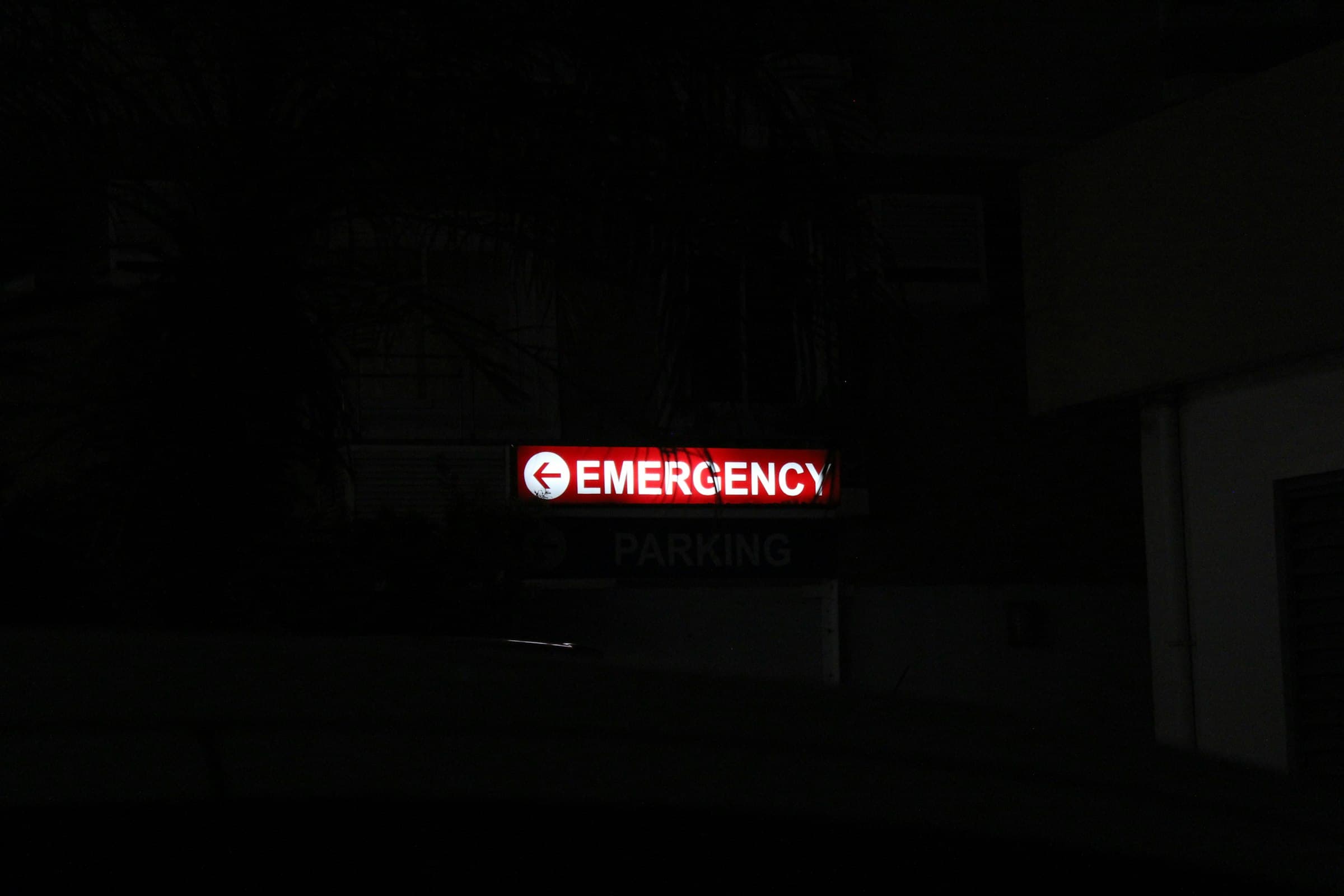 A red EMERGENCY sign glowing in the dark outside a hospital at night