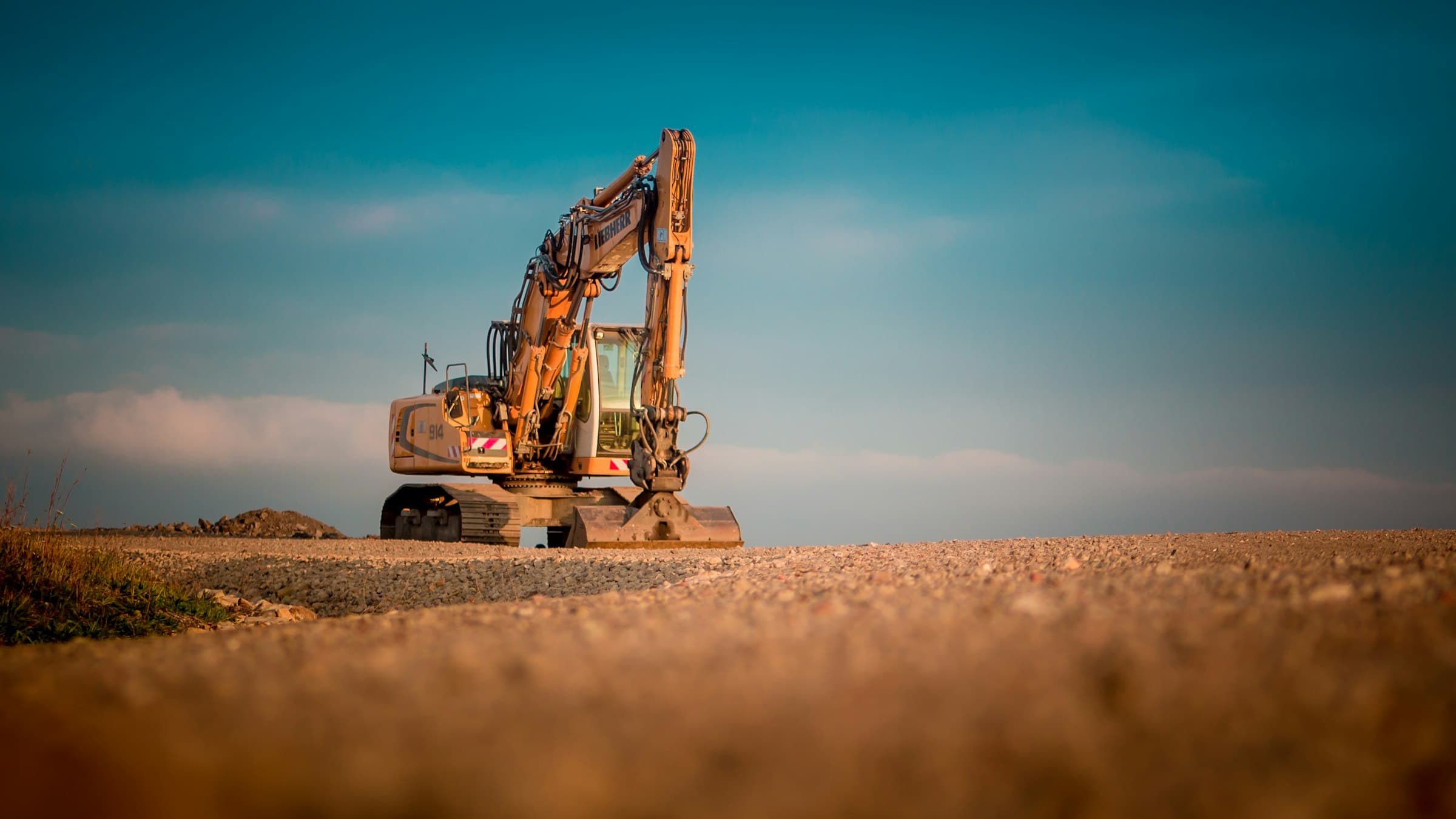 An excavator on a ridge of dirt against a teal evening sky