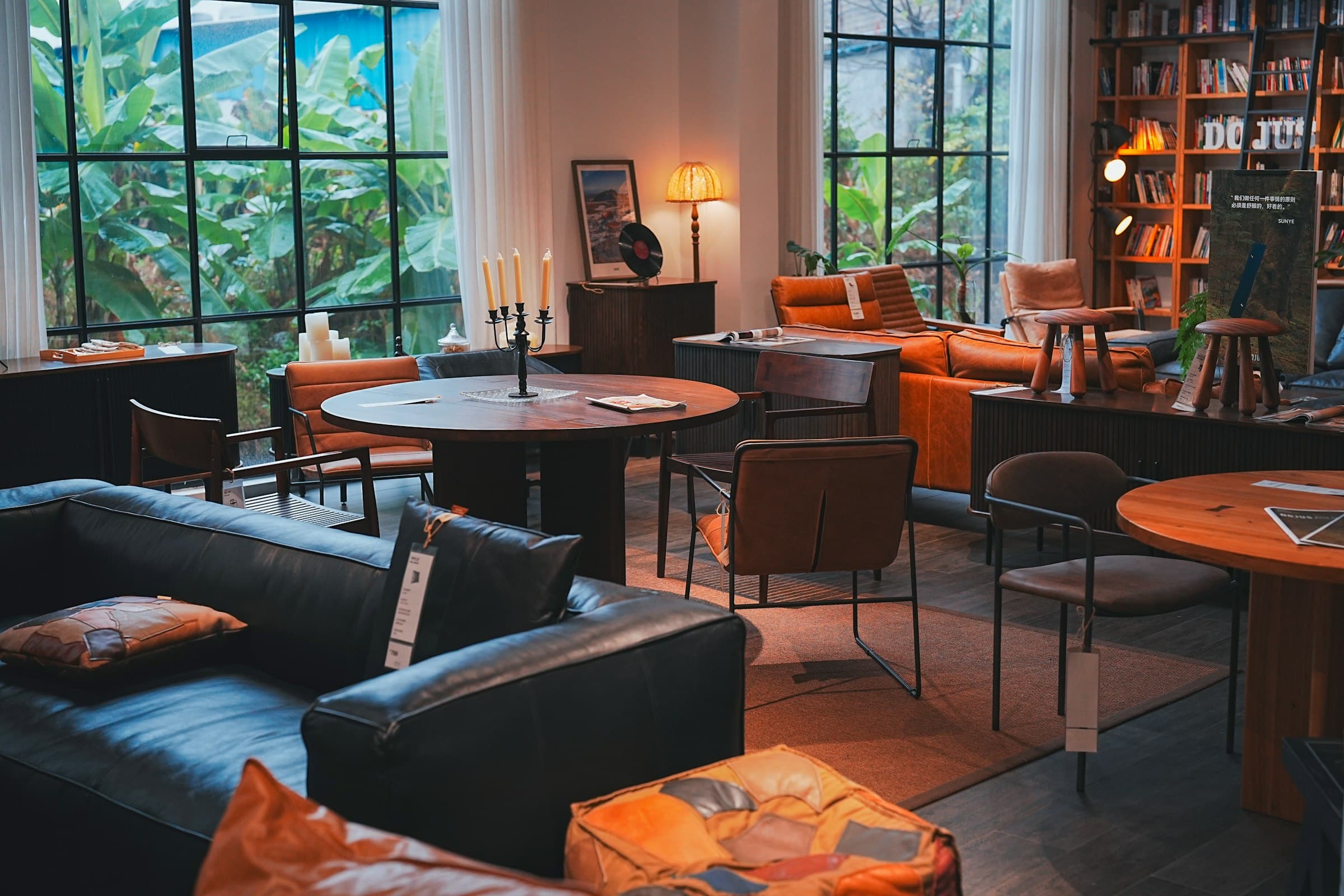 A furniture showroom with leather sofas, round tables and lamps by tall windows