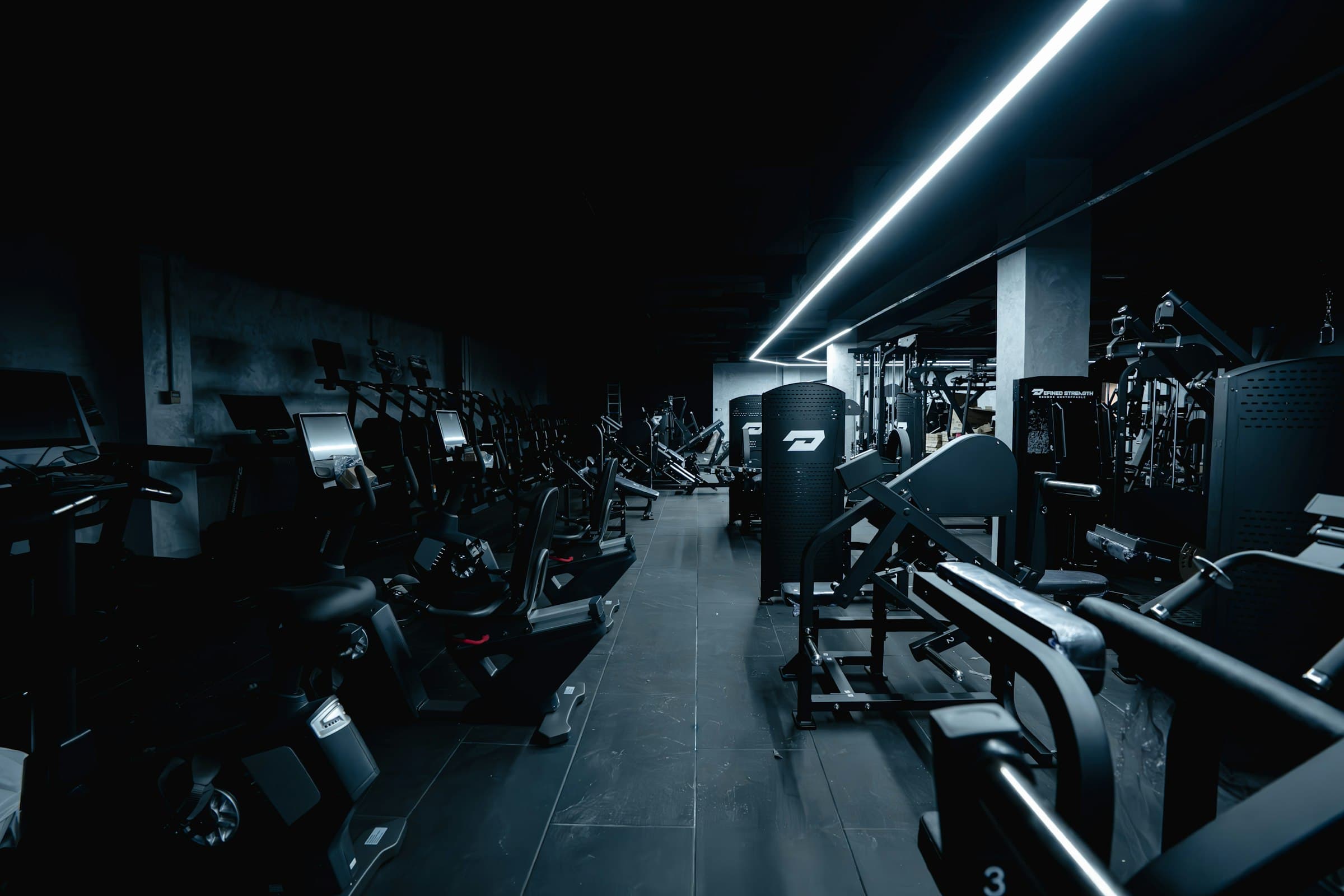 Rows of gym machines in the dark under a single streak of light