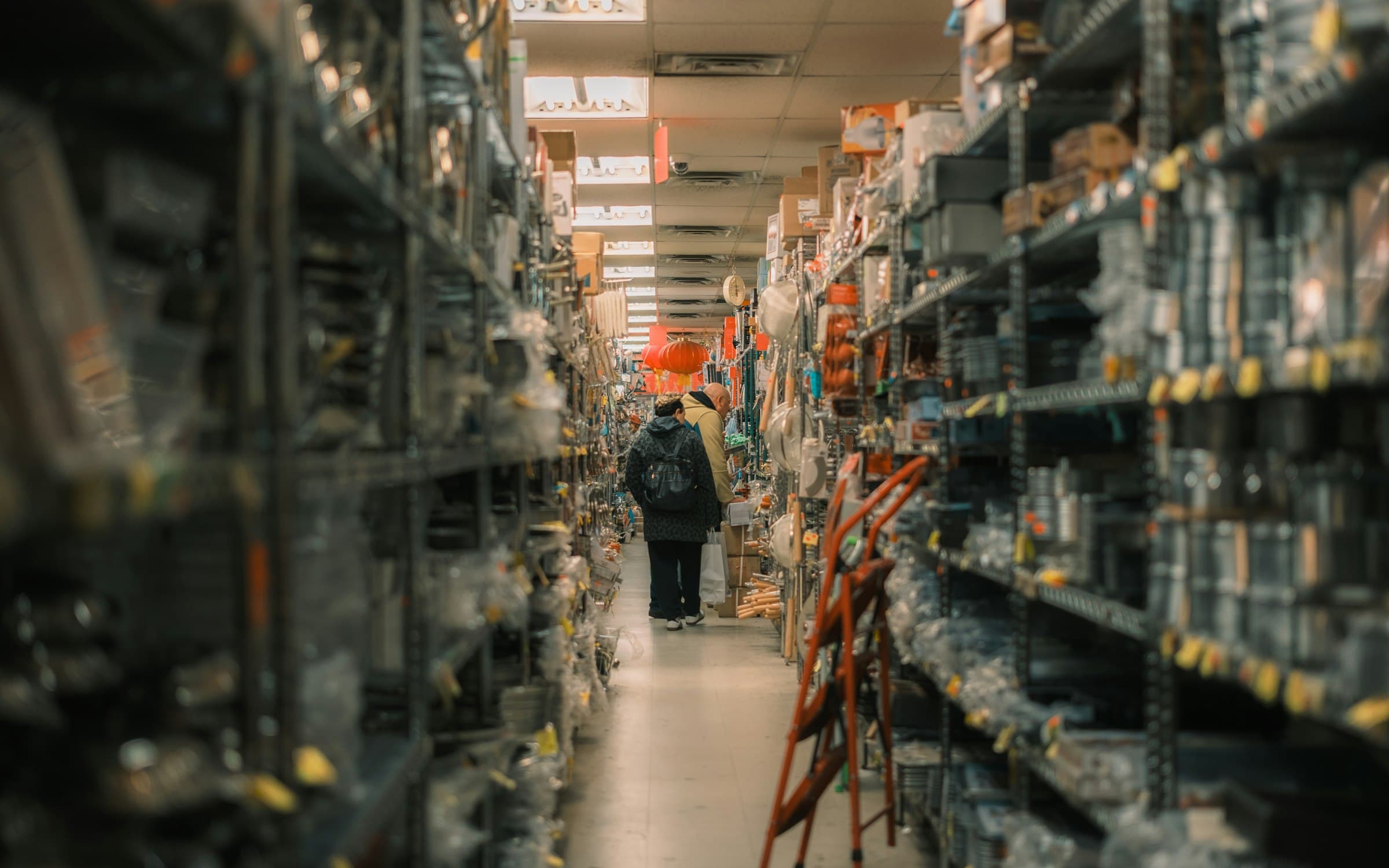 A narrow hardware store aisle packed floor to ceiling, a shopper at the far end