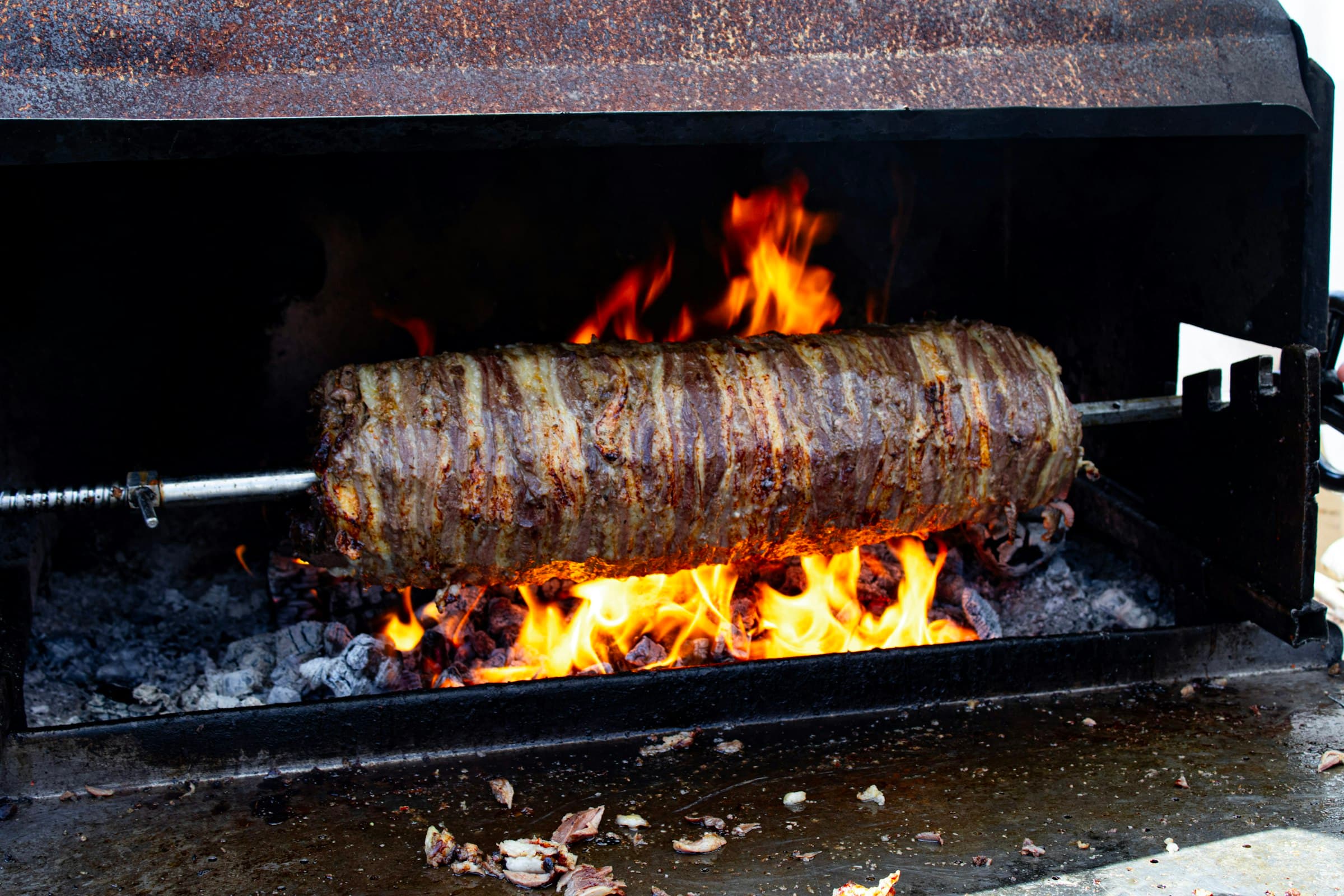 A horizontal spit of kebab meat roasting over an open wood fire