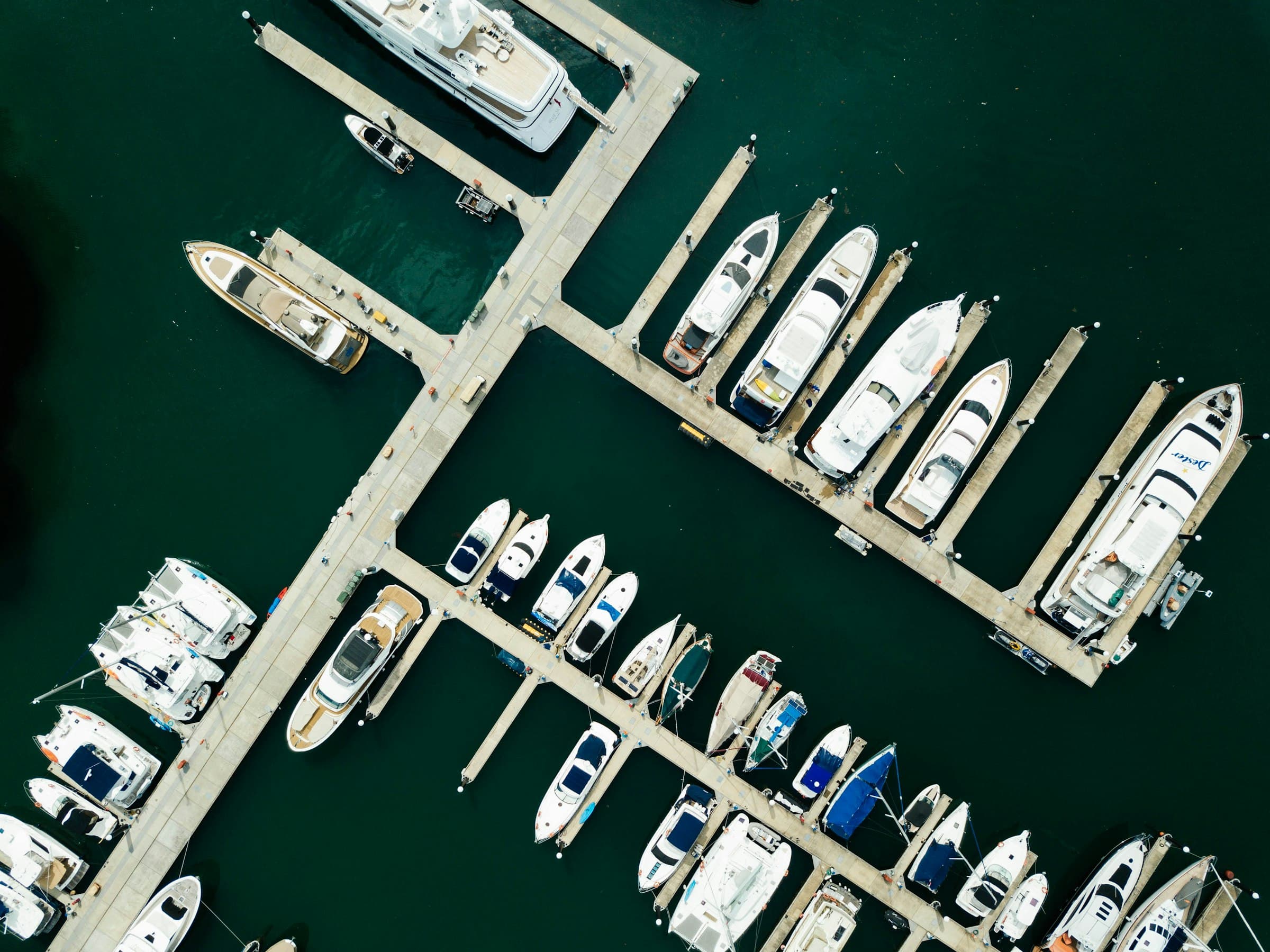 Boats tied up along a marina's docks, seen from above over dark green water