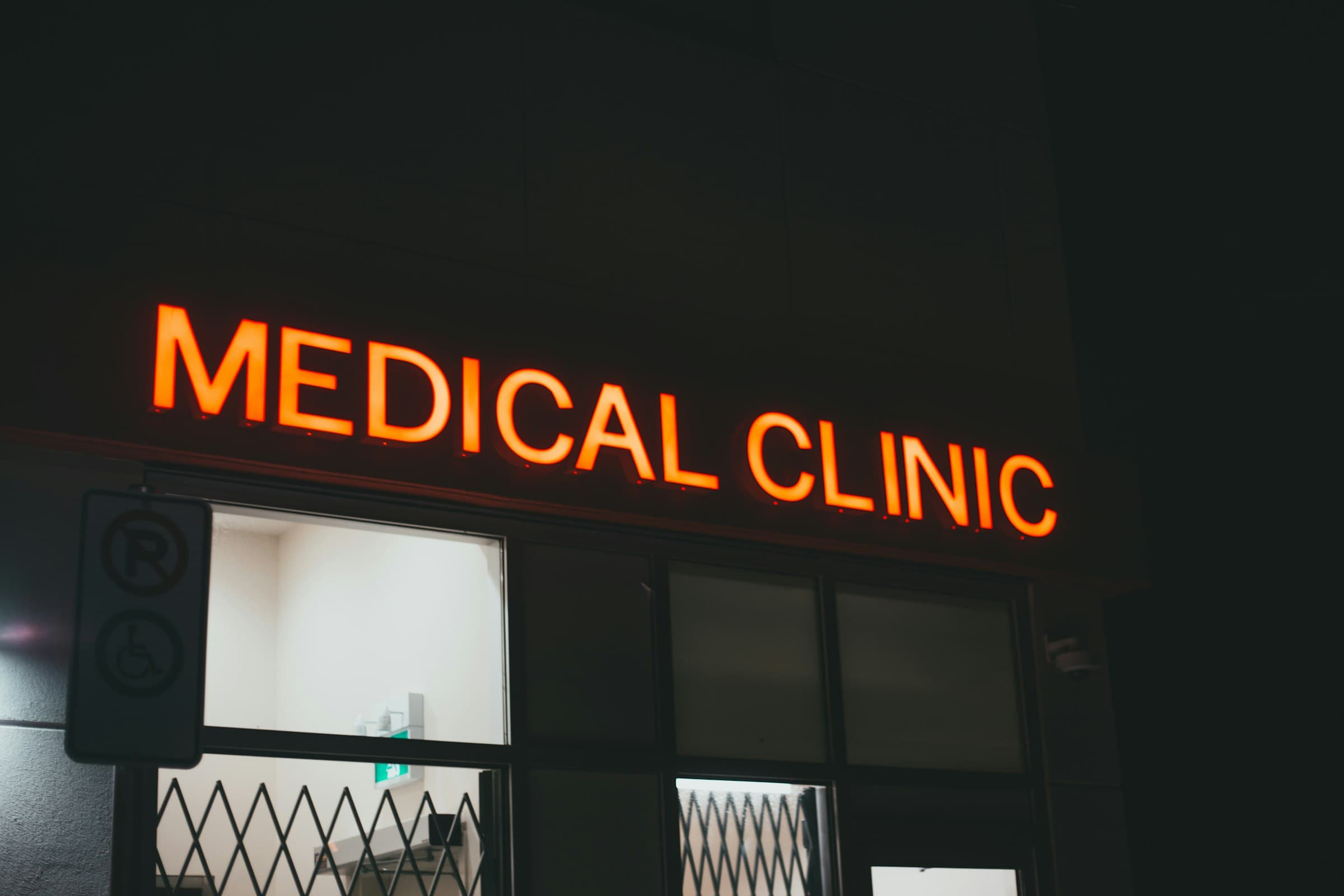 An orange lit MEDICAL CLINIC sign above a clinic's windows at night