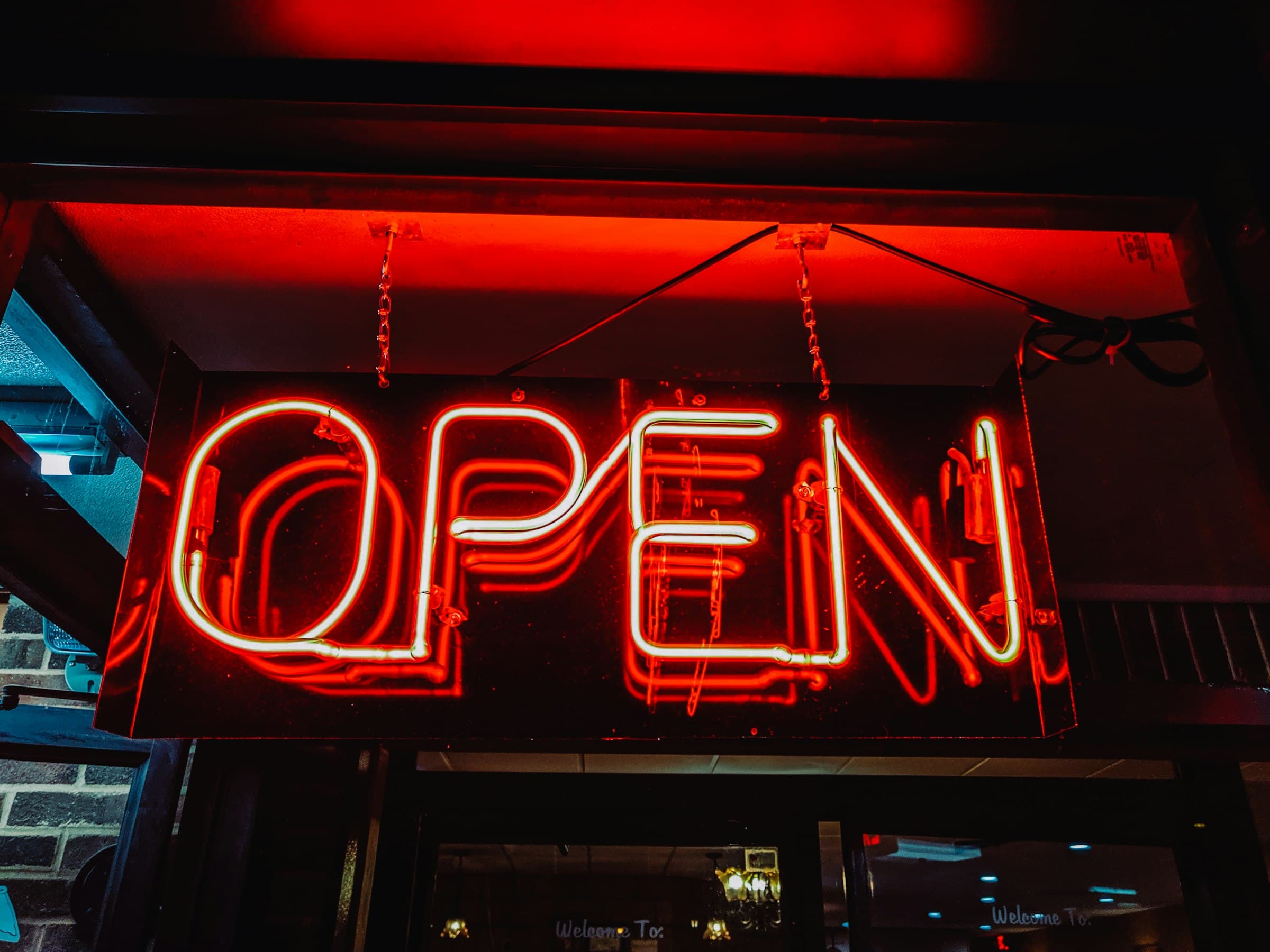 A red neon OPEN sign hanging under a shop's awning at night