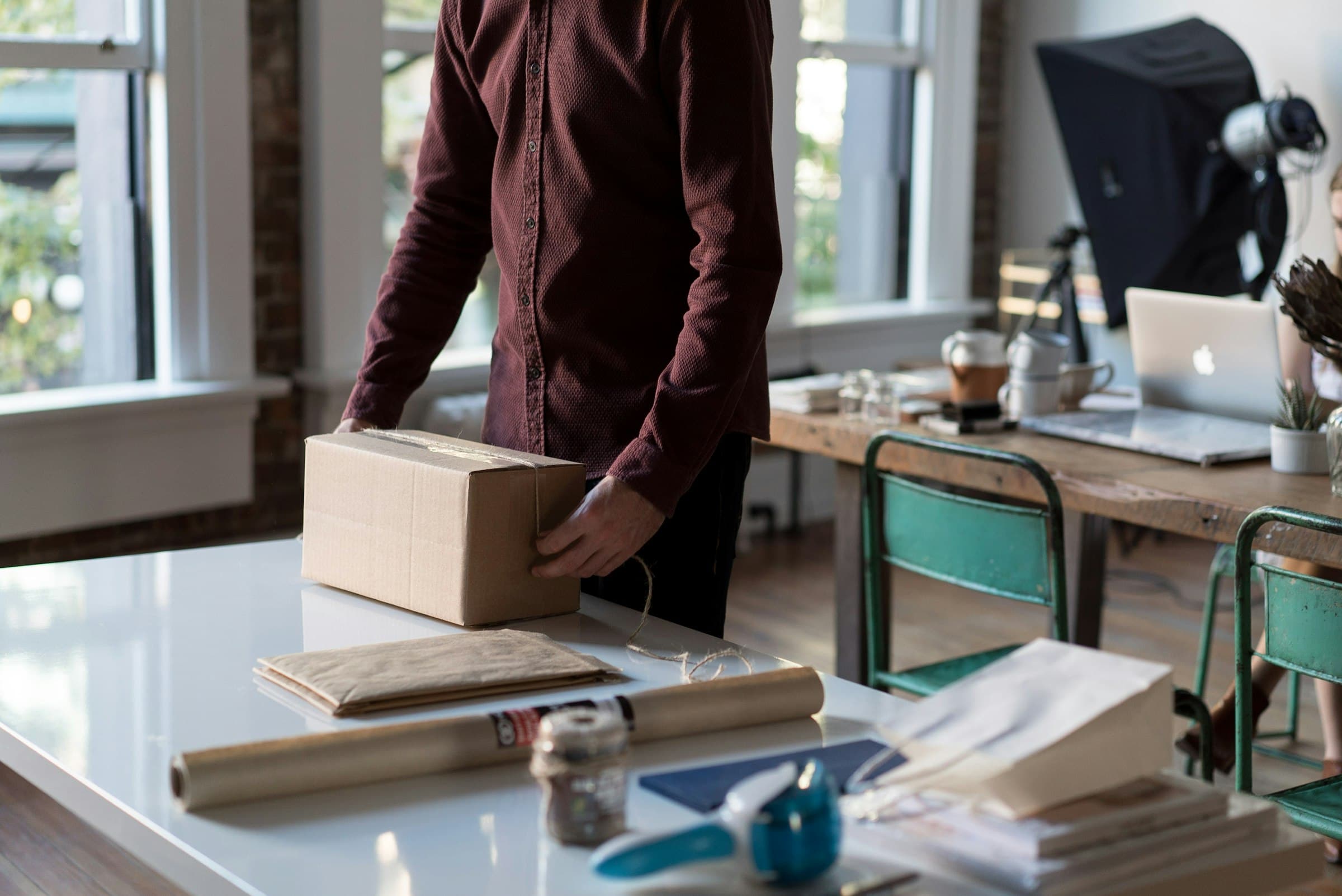 A person packing an order into a cardboard box at a desk beside a laptop
