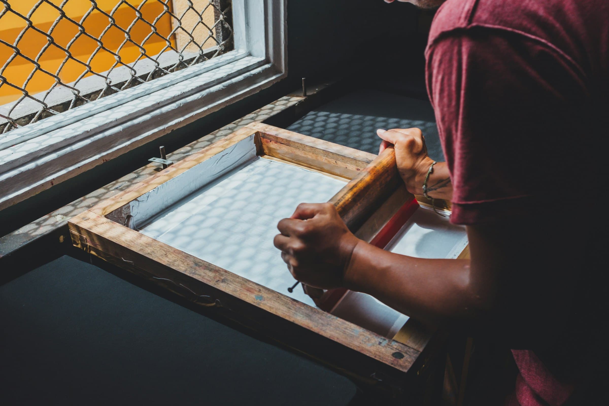 Hands pulling a squeegee across a screen-printing frame