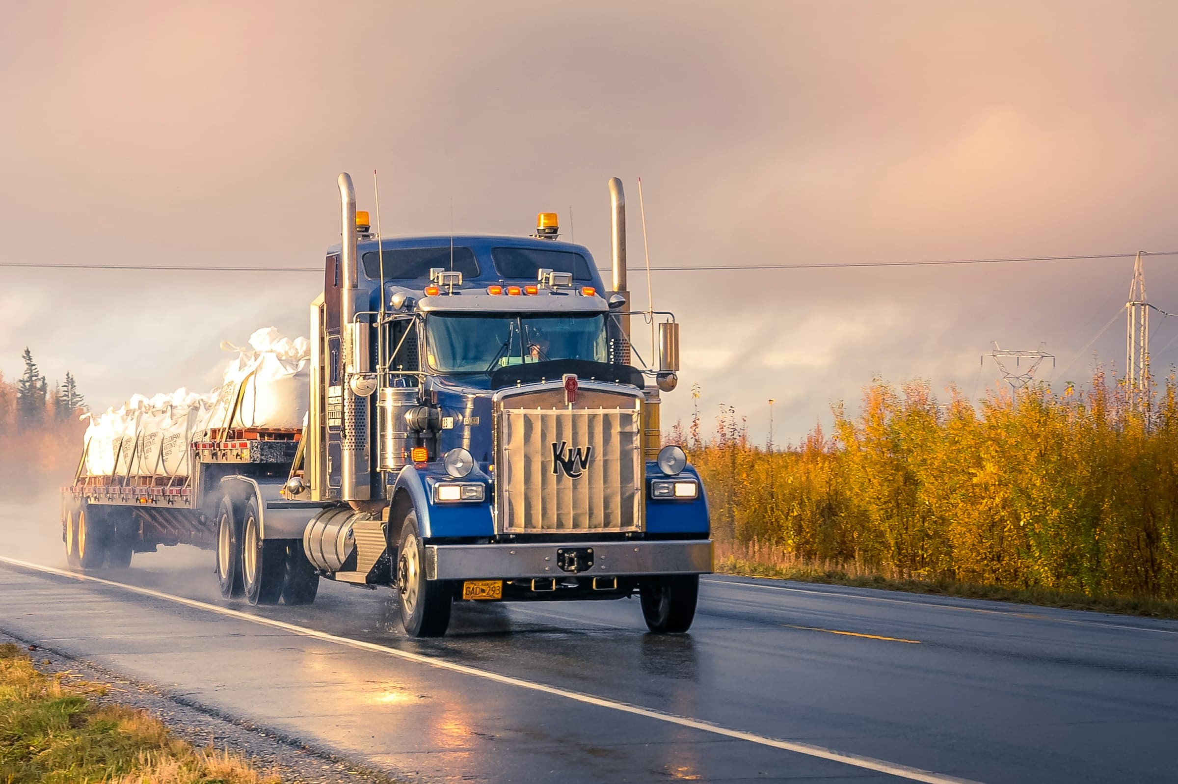 A chrome-grilled semi truck on a wet road at dusk