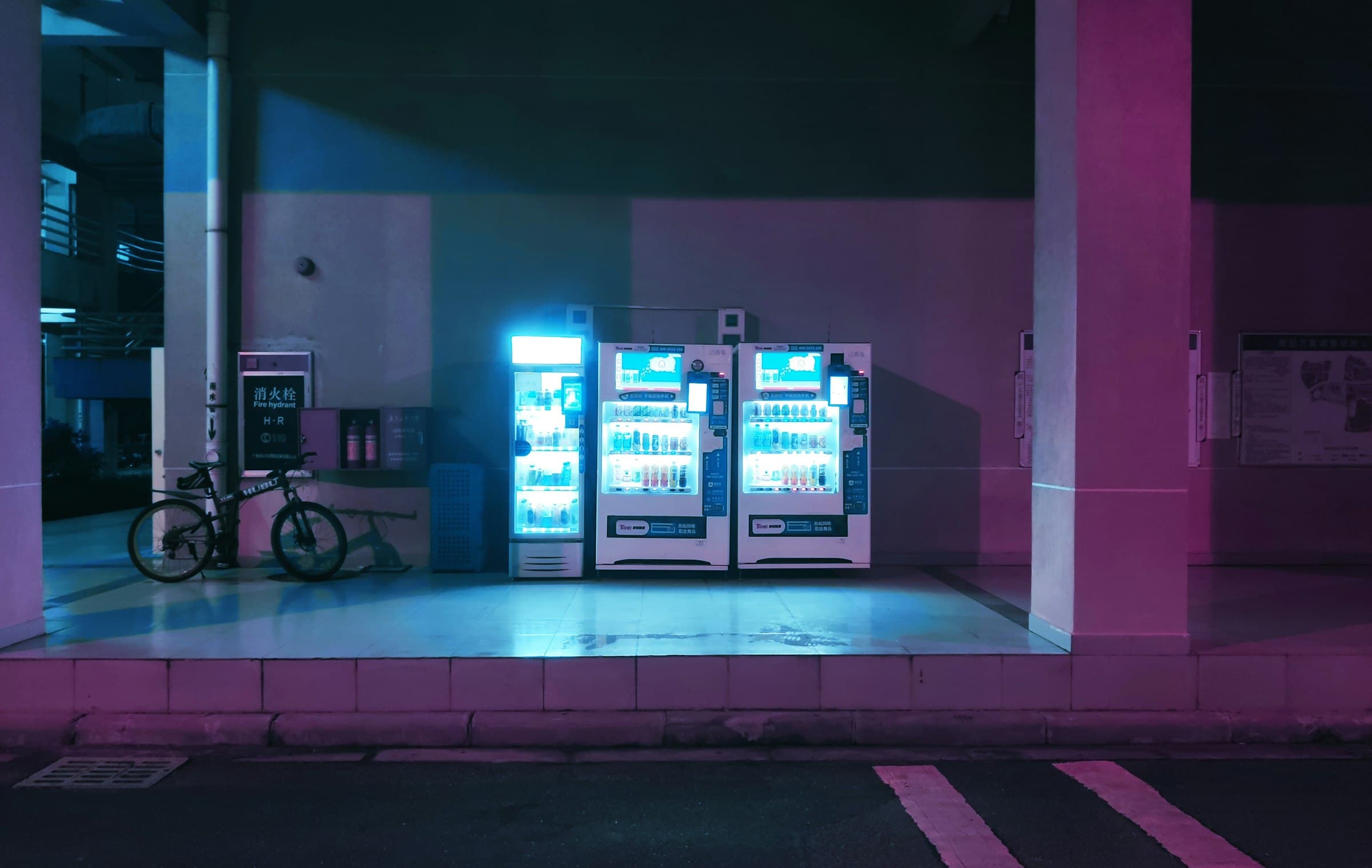 Three lit vending machines at night in pink and blue light