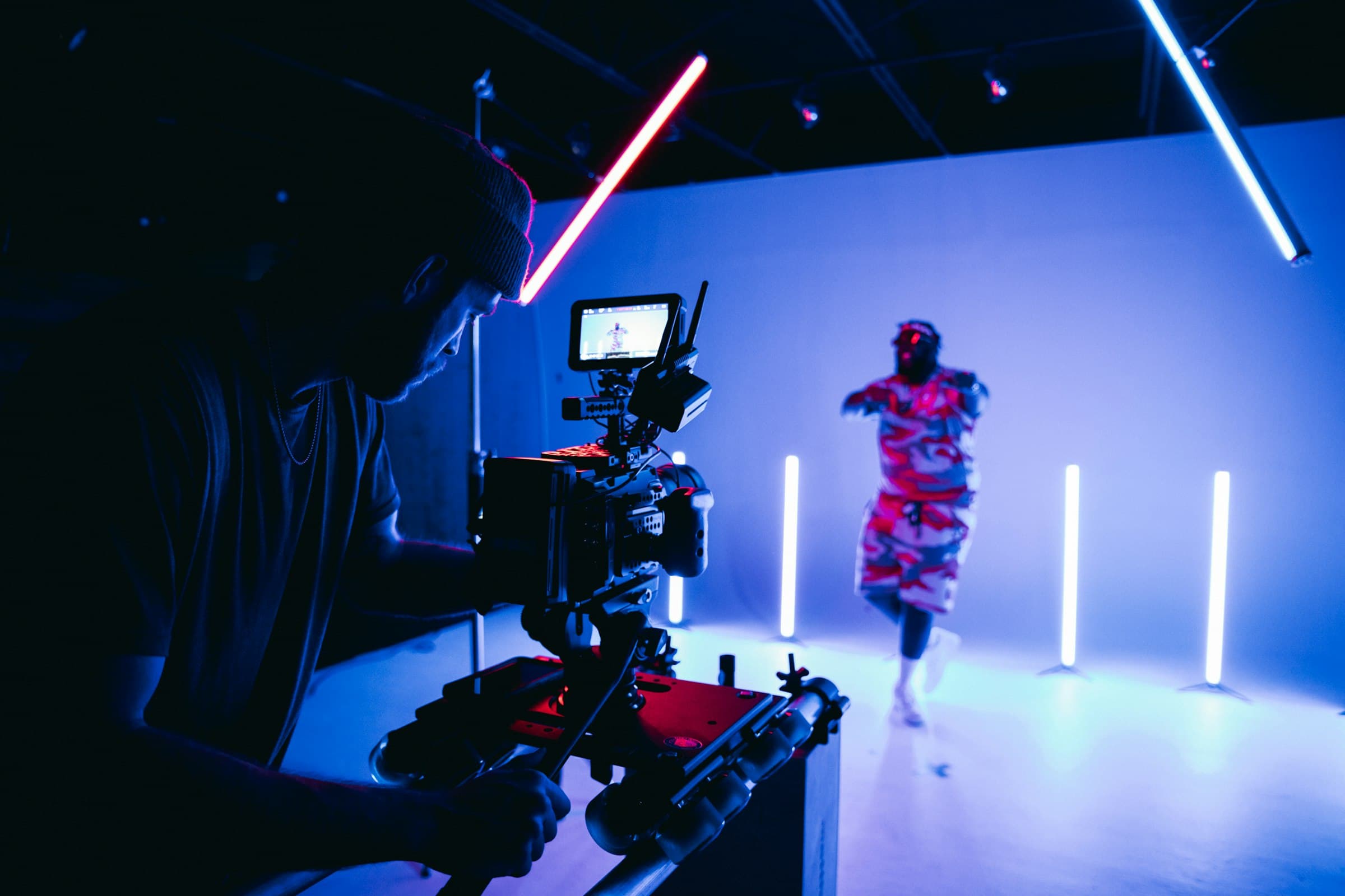 A camera filming a dancer in a studio lit by neon tubes