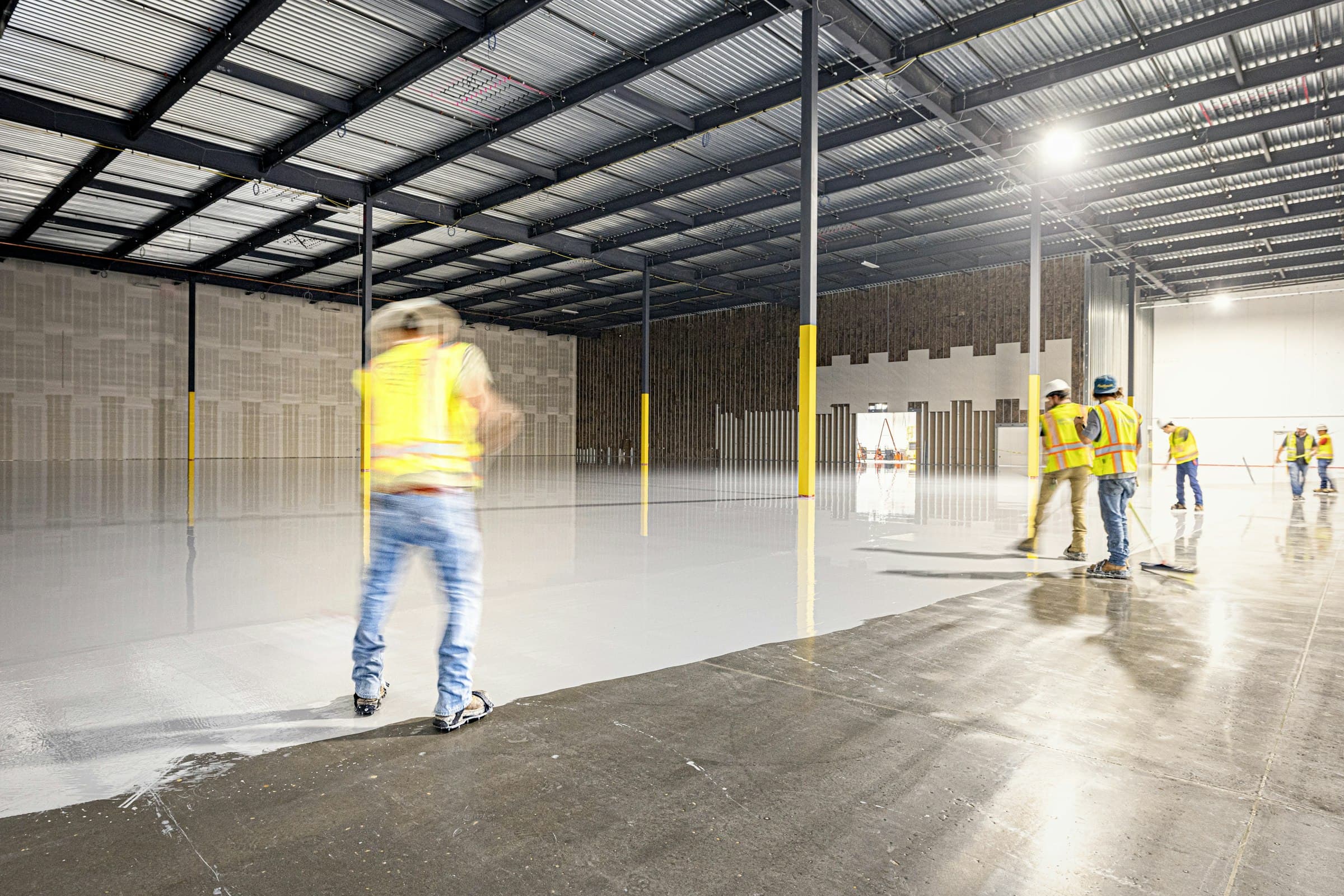A crew spreading a glossy coating across a warehouse floor