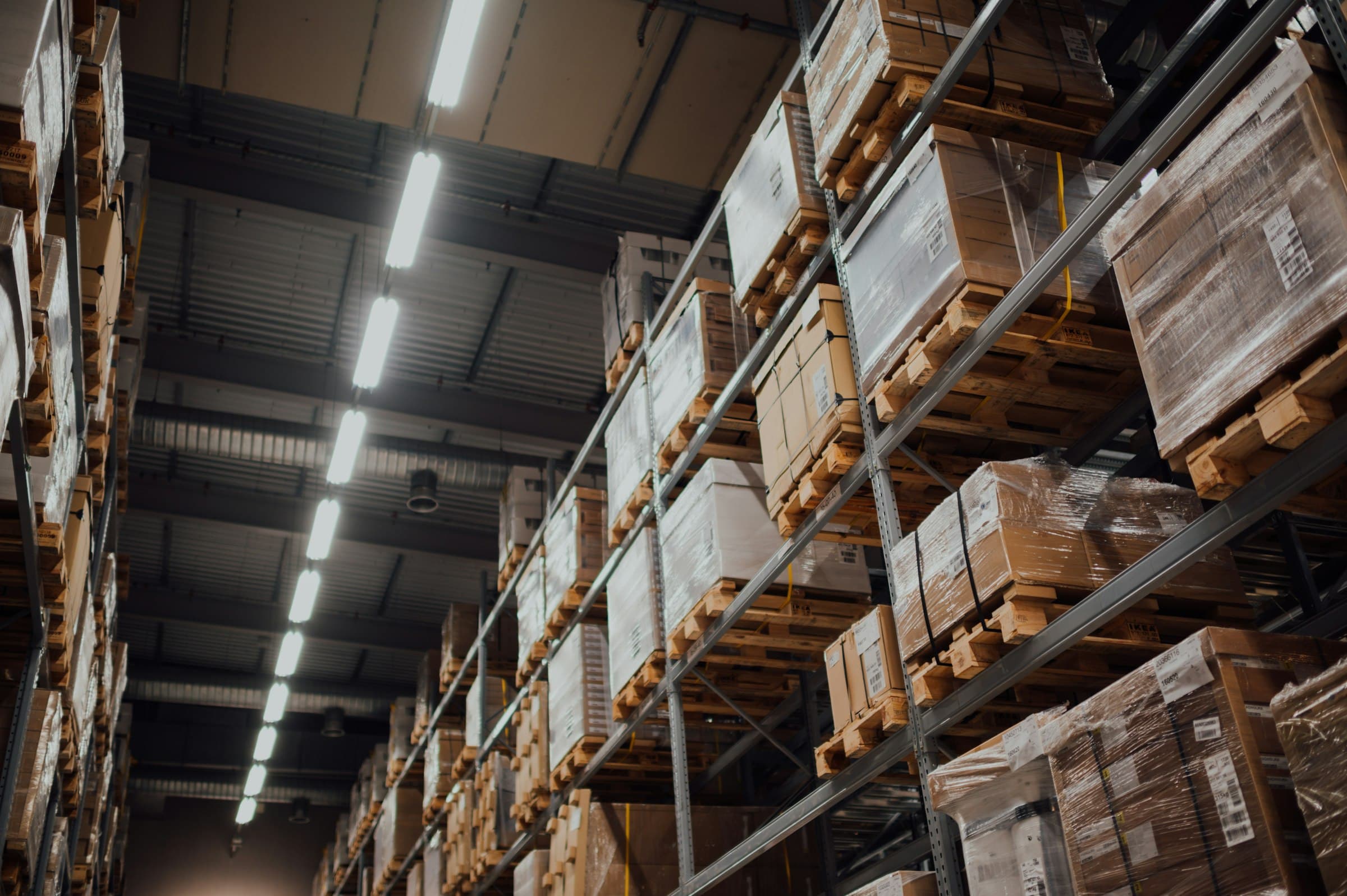 Pallets of boxes stacked high on warehouse racks under strip lights