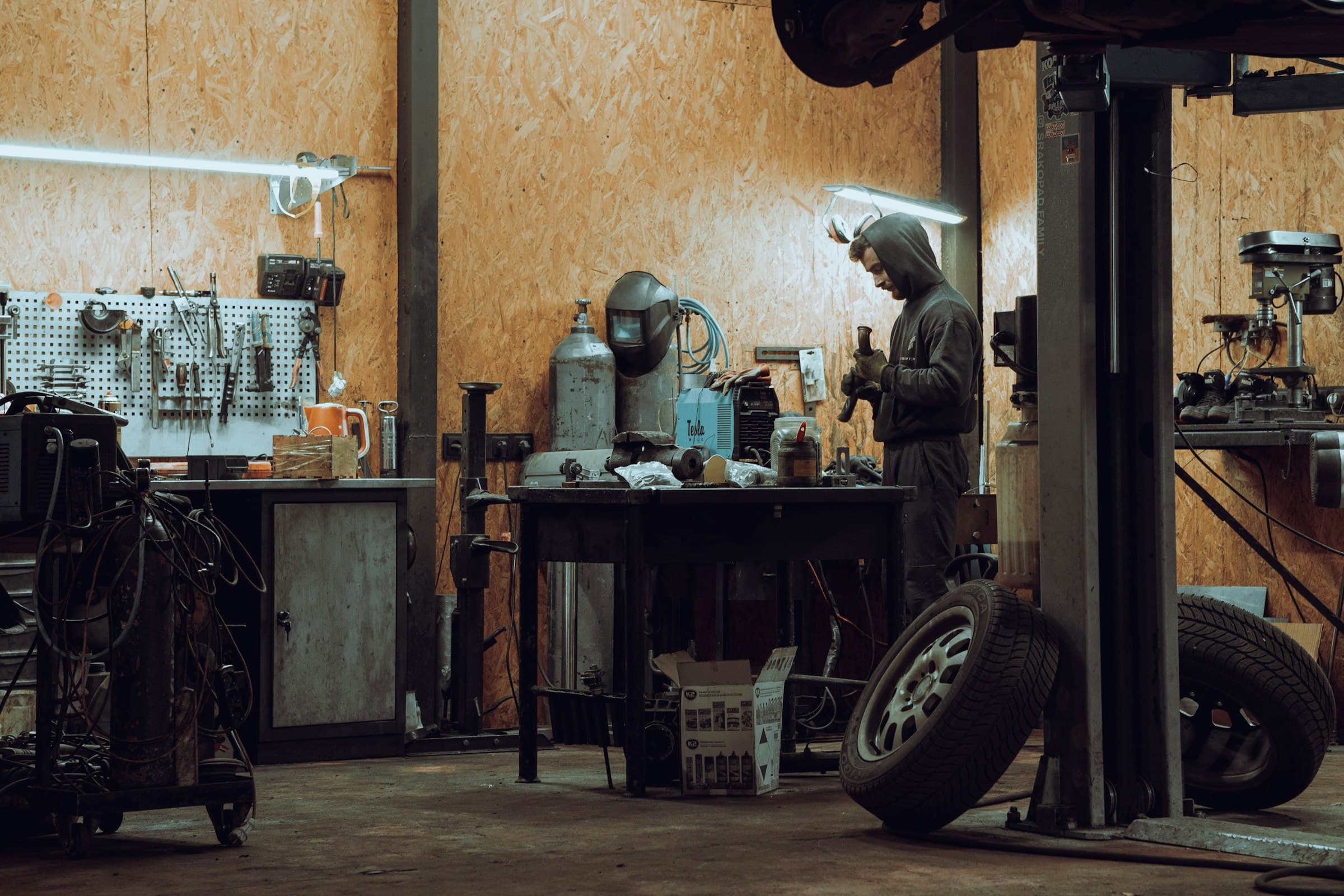 A mechanic at work in a dim garage, tools on the wall and tires on the floor