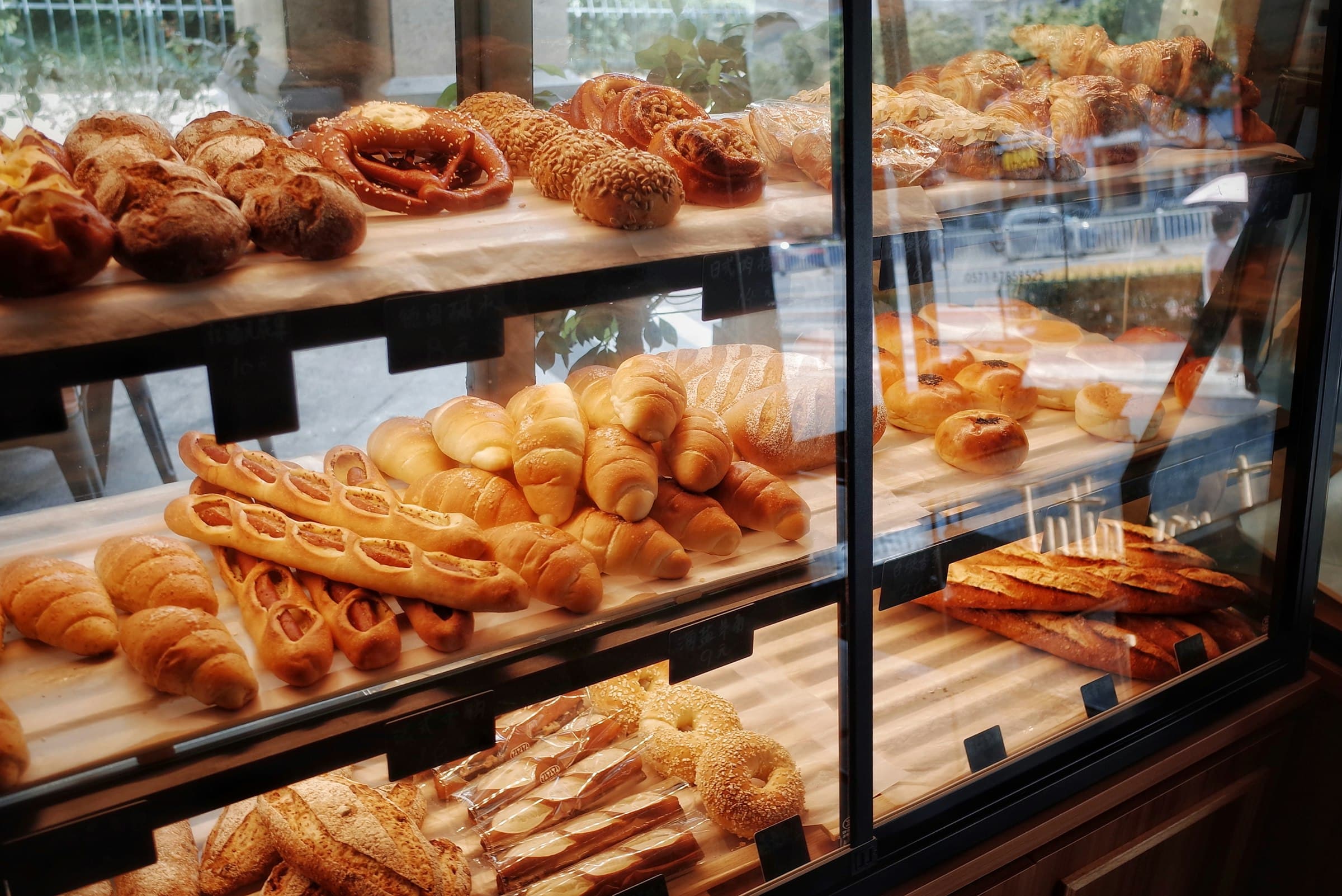 A bakery's glass case stacked with croissants, twisted pastries and loaves