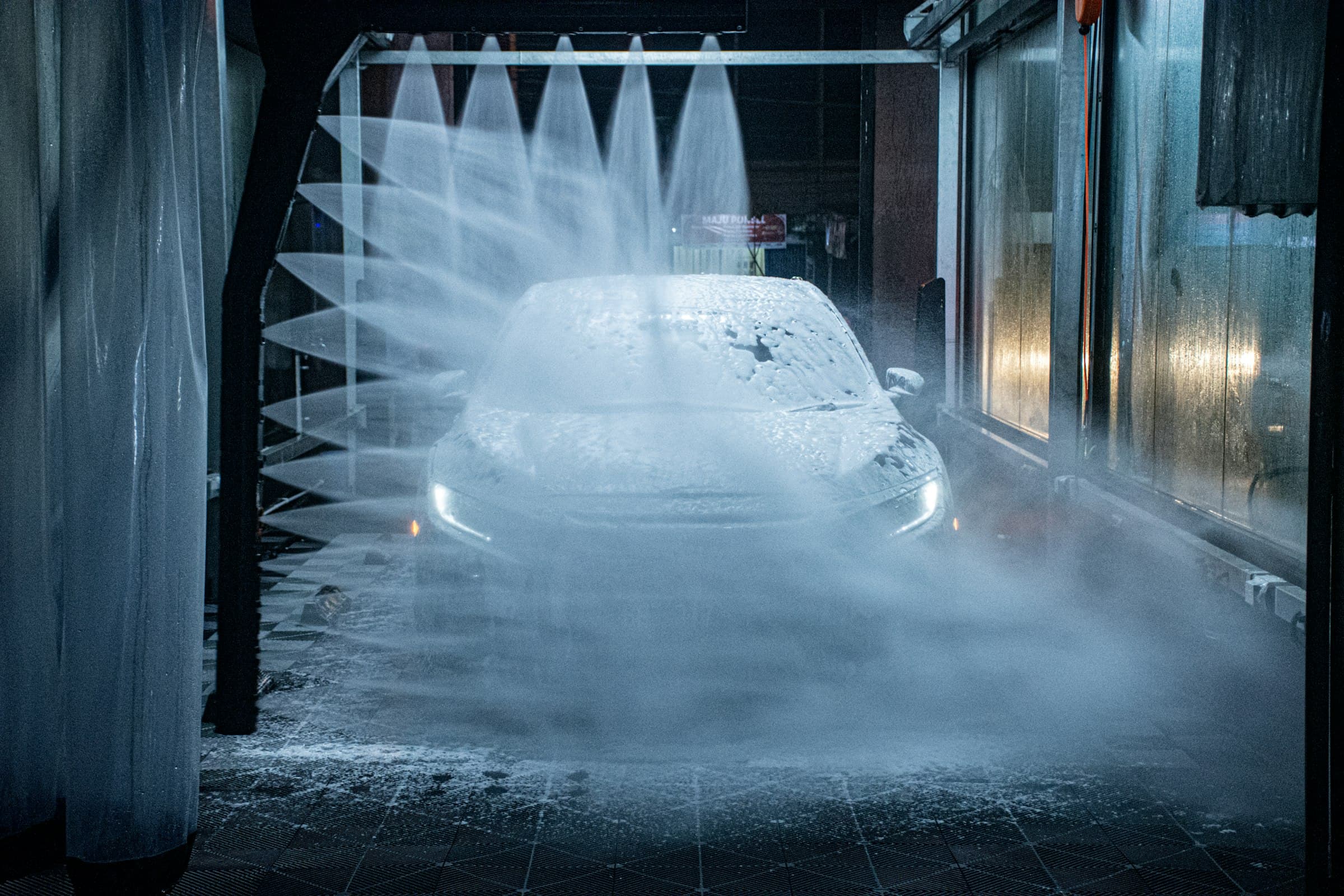 A car in a wash bay under arches of high-pressure spray, lit blue in the dark