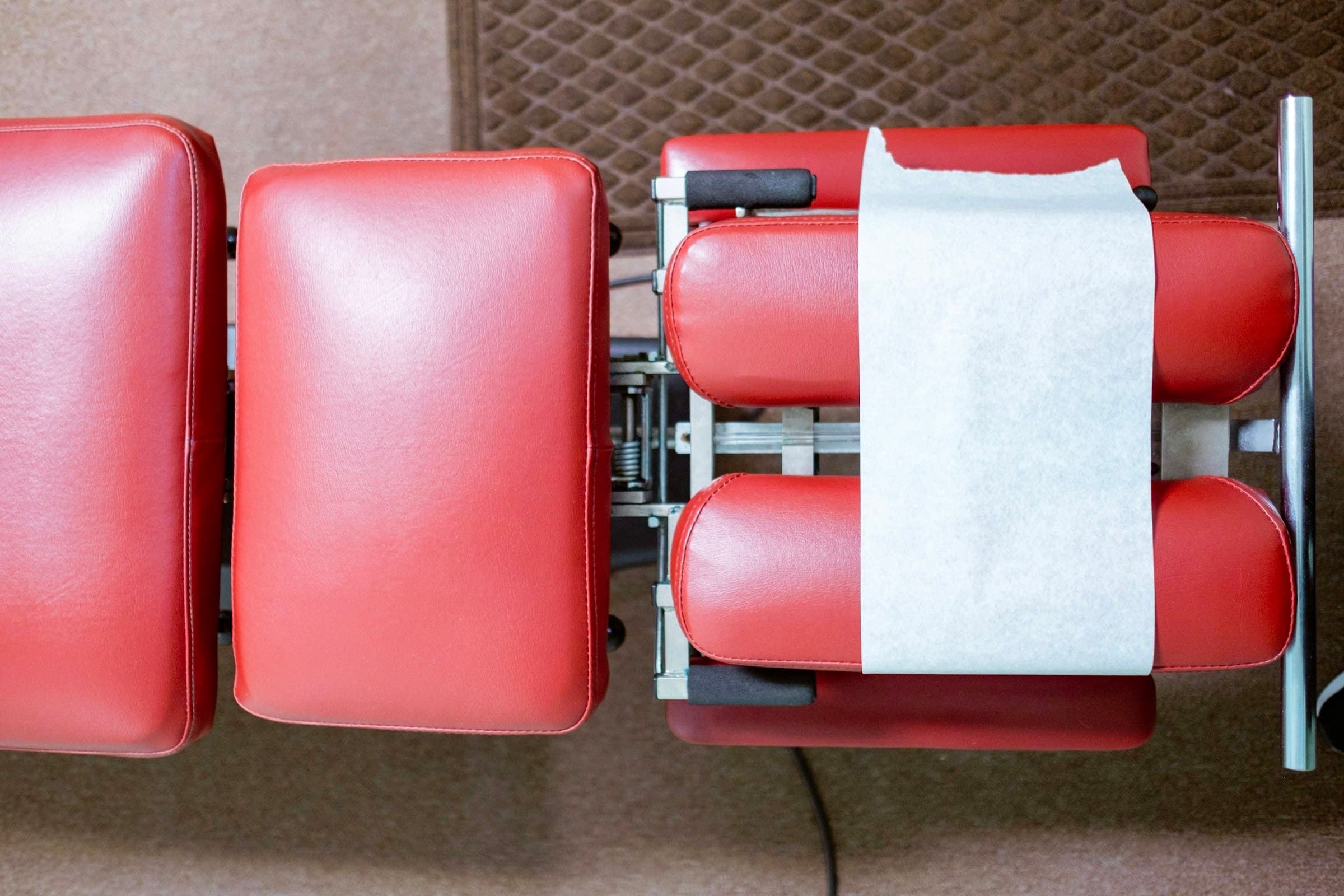 A red chiropractic adjusting table seen from above, its headrest covered in paper