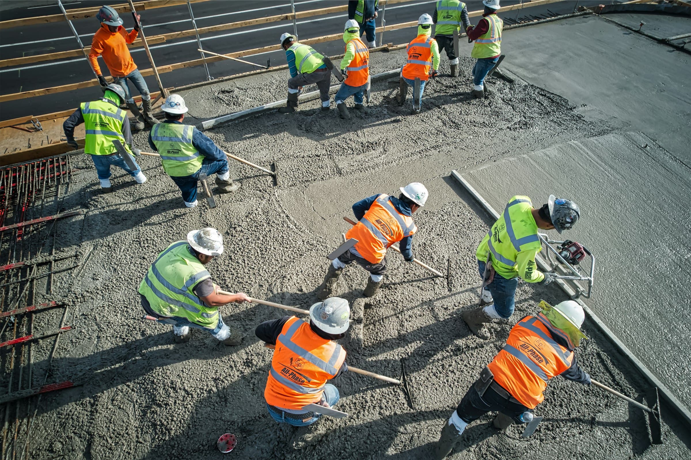 A crew in hard hats and high-visibility vests raking wet concrete, seen from above