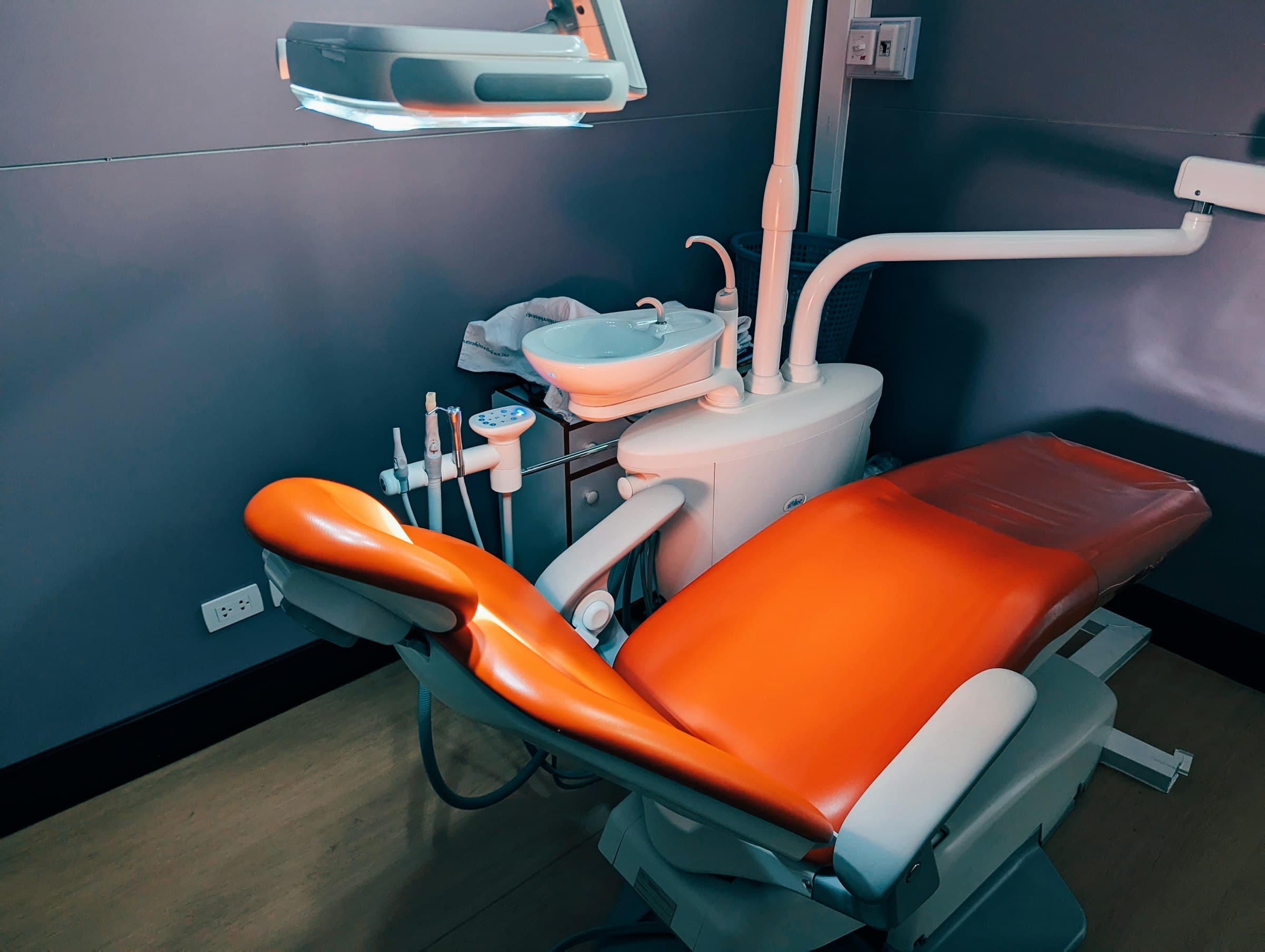An orange dental chair and its lamp against a dark teal wall in a dental office