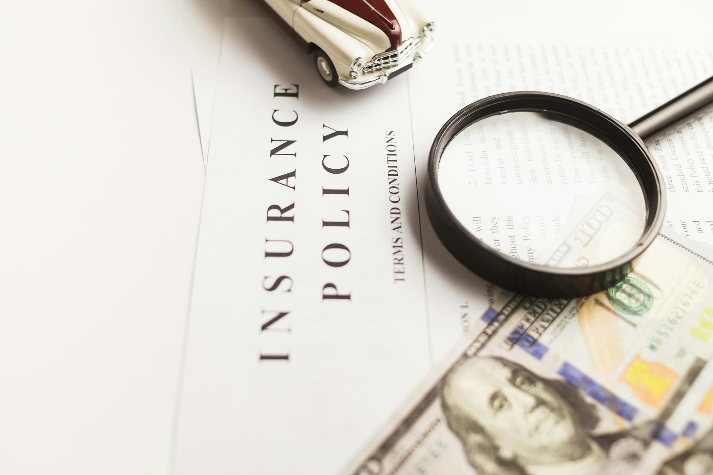 An insurance policy under a magnifying glass, with a toy car and banknotes