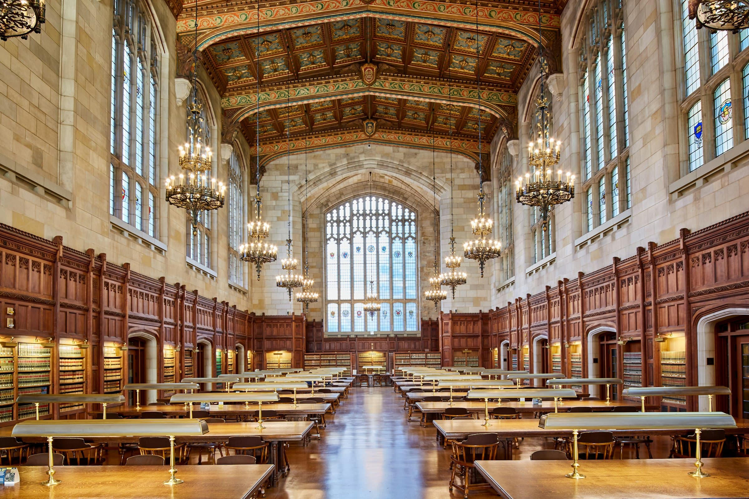 A Gothic law library reading room with chandeliers, long tables and tall arched windows