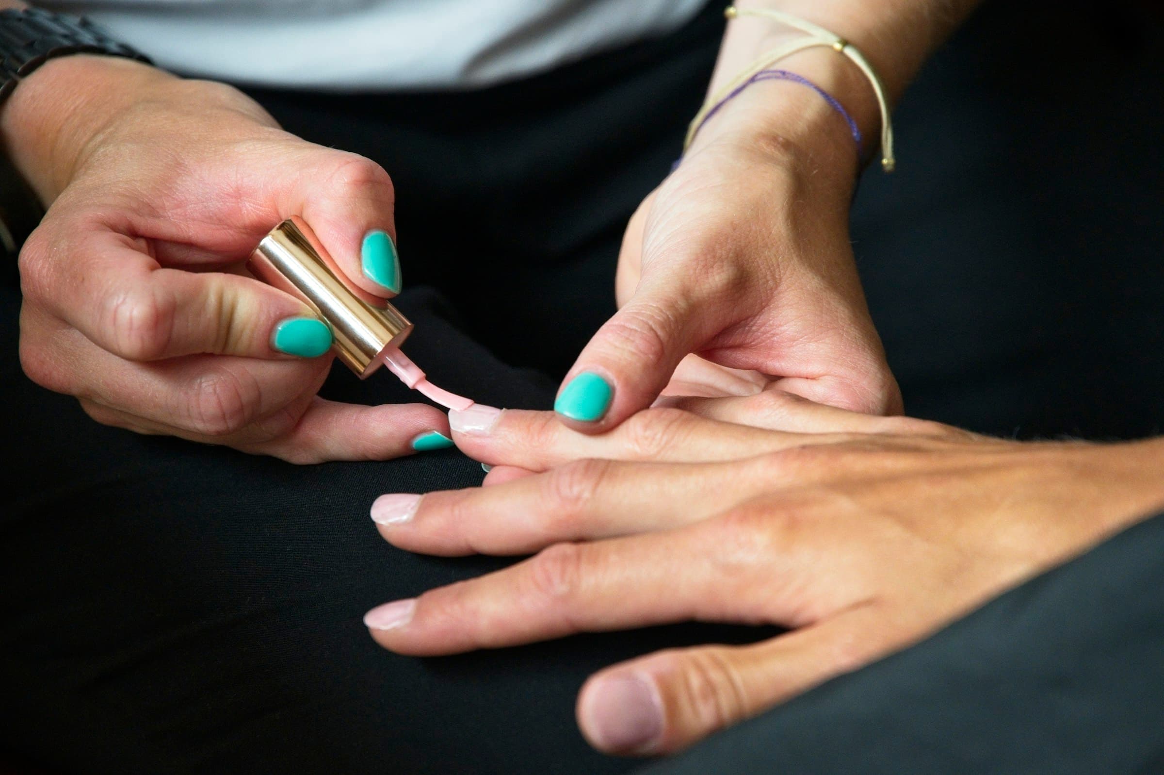 A nail technician painting a client's nails teal