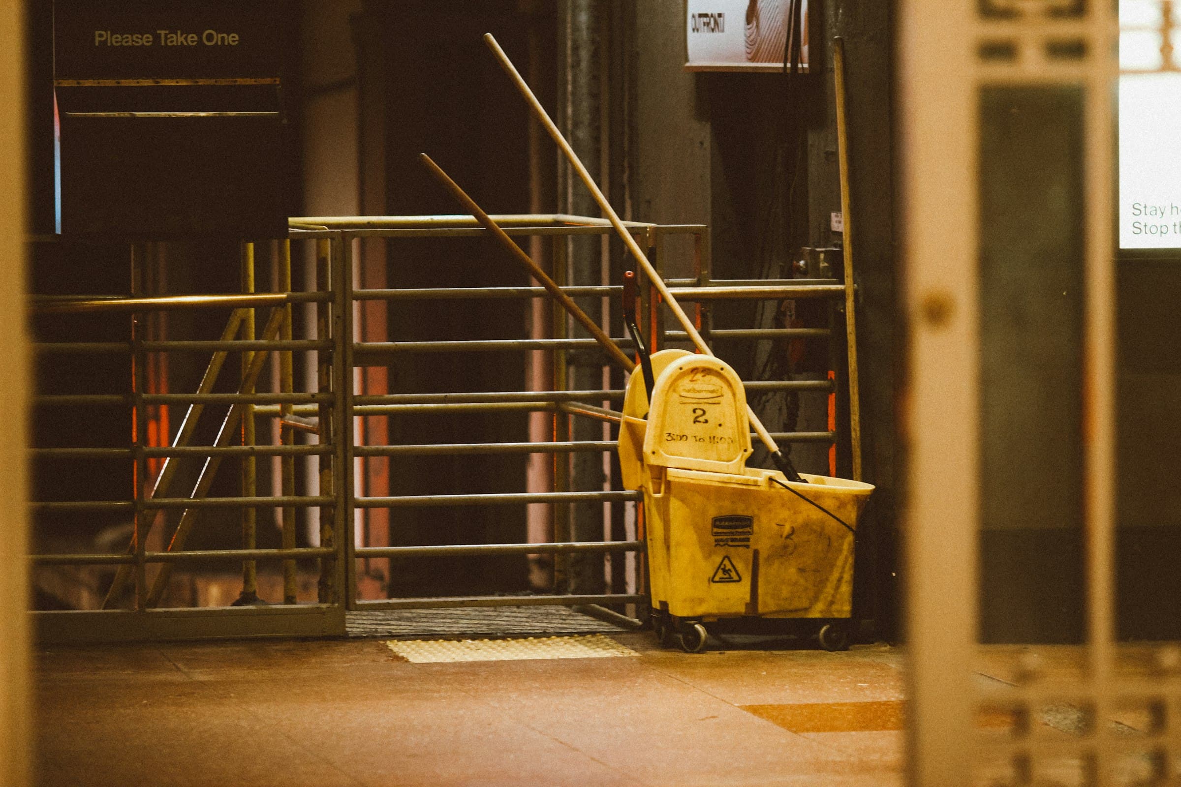 A yellow mop bucket beside turnstiles in a dim lobby after hours