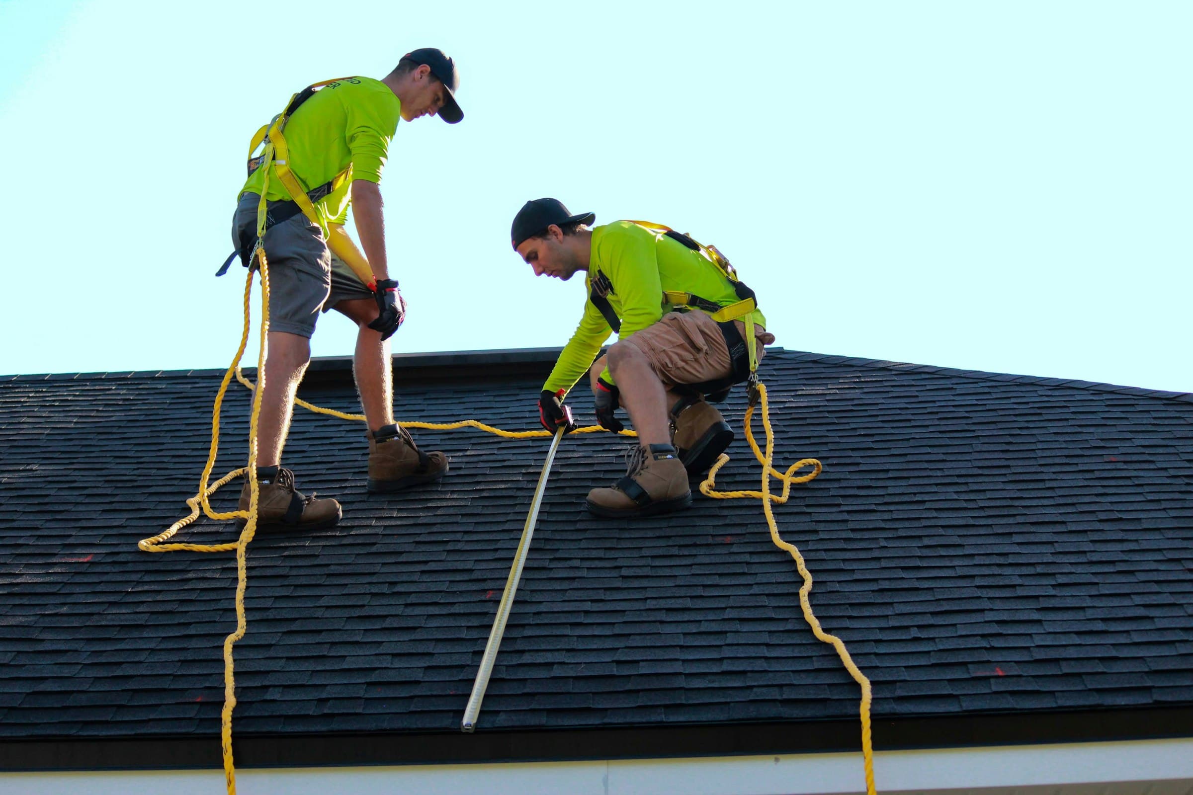Two roofers in safety harnesses working across a shingle roof