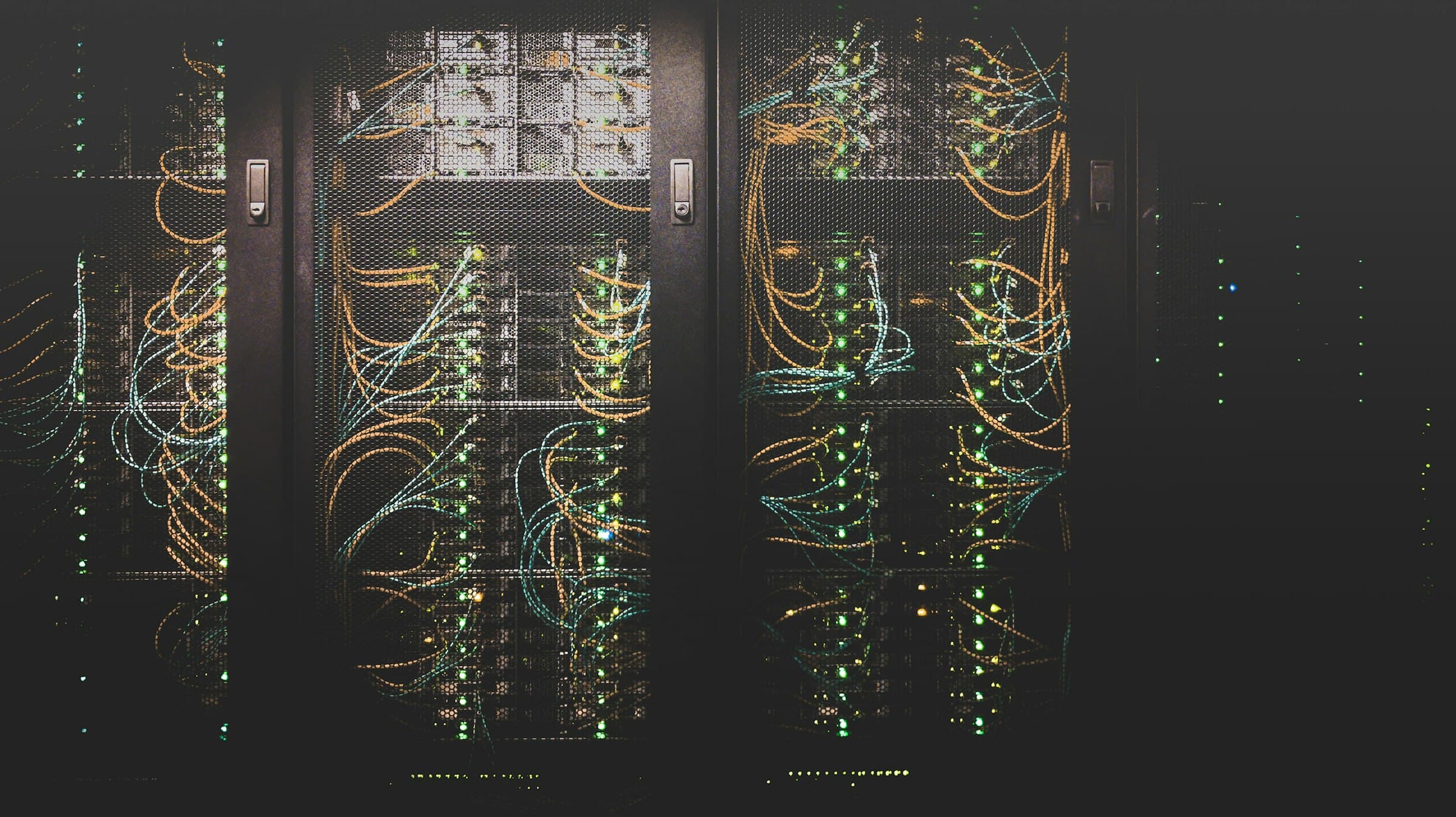 Server racks in a dark data center, fiber cables and green status lights behind mesh doors