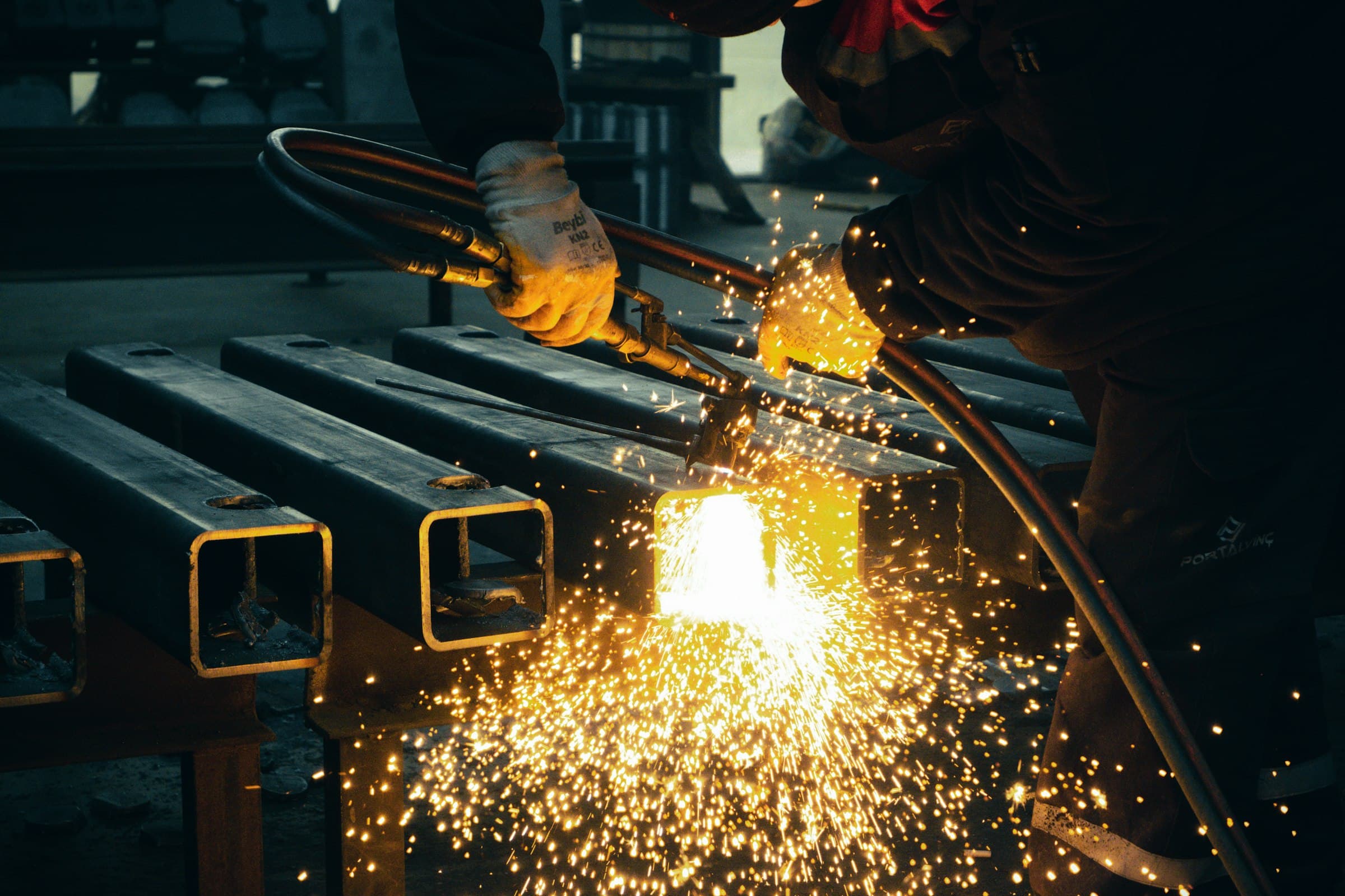 A torch cutting square steel tube in a shower of sparks